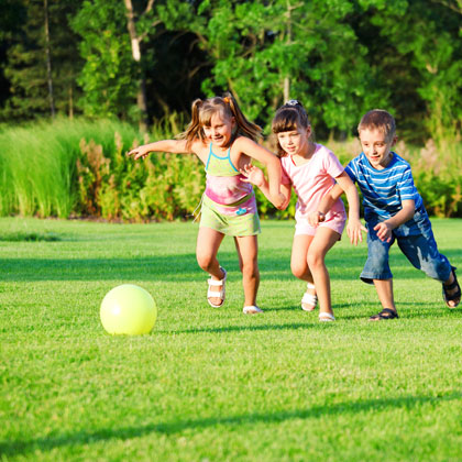photo de 3 enfants, 2 filles et 1 garçon  jouant dans un jardin avec un ballon jaune